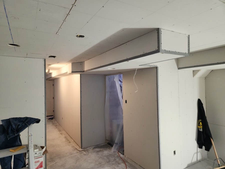 A boarded and taped bulkhead and hallway in a basement renovation by JW Drywall