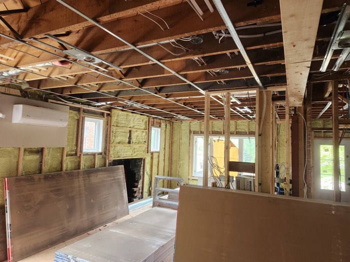 A main floor stripped to the studs with drywall sheets stacked ready to hang