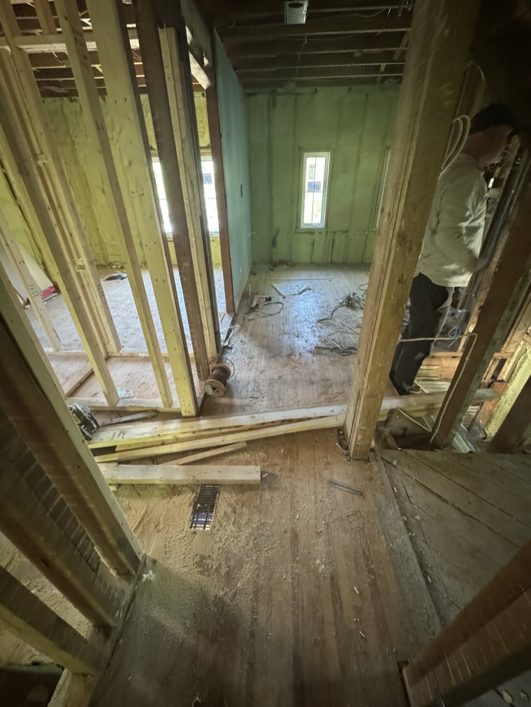 A tradesperson working inside an open wall beside new stud framing